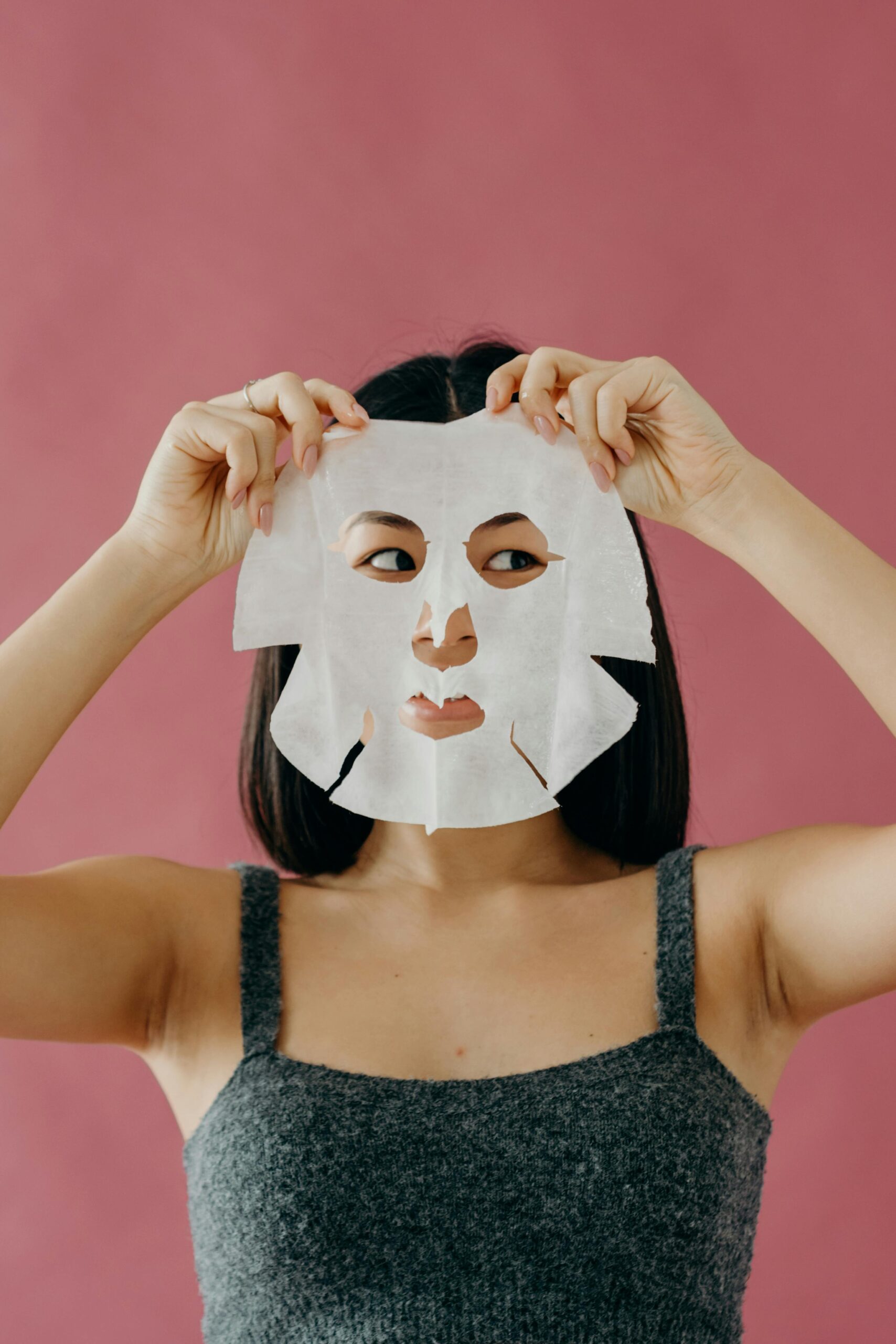 A woman holding a sheet mask over her face, highlighting skincare and self-care routines.